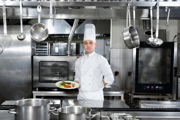 Chef in a restaurant holds a plate with a ready-made dish