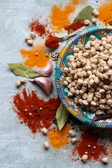 Obraz na płótnie Canvas Raw chick-peas on blue ceramic plate, paprika powder, turmeric, pepper and bay leaf top view photo. Colorful still life with different spices. Mediterranean culture concept. 