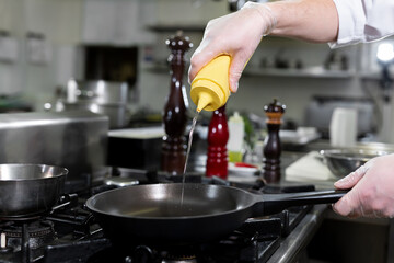 Chef pours olive oil from a bottle into a frying pan