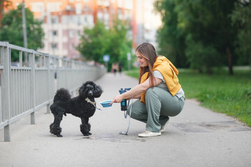 cute european girl on walk gives her dog water from bottle and bowl, taking care of pet. Woman and...