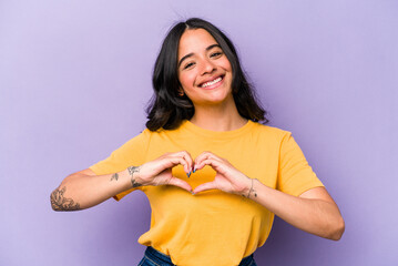 Young hispanic woman isolated on purple background smiling and showing a heart shape with hands.