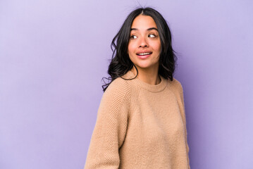 Young hispanic woman isolated on purple background looks aside smiling, cheerful and pleasant.