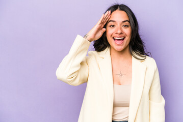 Young hispanic woman isolated on purple background shouts loud, keeps eyes opened and hands tense.