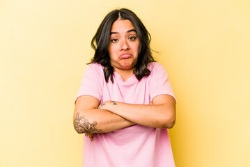 Young hispanic woman isolated on yellow background shrugs shoulders and open eyes confused.