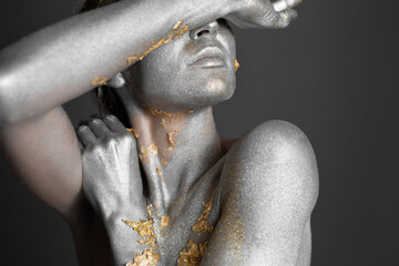 Portrait of a beautiful female model with gold and silver paint on her skin and hair in the studio.