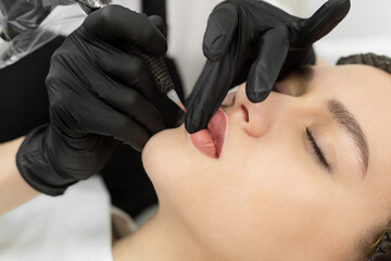 Close-up of the permanent makeup procedure. Lip makeup in the cosmetologist's salon. - obrazy, fototapety, plakaty