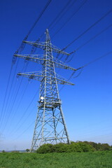 Einzelner Hochspannungsmast vor einem blauen Himmel