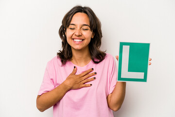 Young hispanic woman holding a beginner driver sign isolated on white background laughs out loudly keeping hand on chest.
