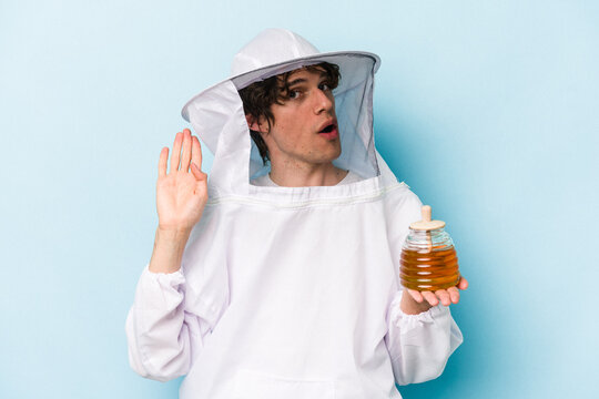 Young caucasian beekeeper man isolated on blue background trying to listening a gossip.