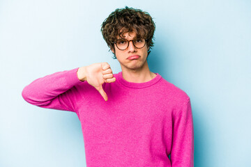 Young caucasian man isolated on blue background showing a dislike gesture, thumbs down....