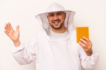 Hispanic beekeeper man holding honey isolated on white background receiving a pleasant surprise, excited and raising hands.