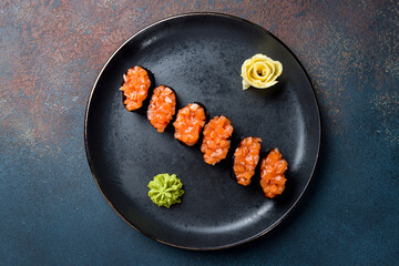 Sushi gunkan with fresh salmon on a black plate on blue concrete table top view