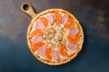 Pizza with ham, mushrooms, tomatoes and red onion with cheese on the board on blue concrete table top view