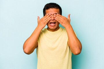 Young hispanic man isolated on blue background covers eyes with hands, smiles broadly waiting for a...