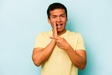 Young hispanic man isolated on blue background saying a gossip, pointing to side reporting...