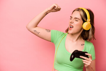 Young caucasian woman playing with a video game controller isolated on pink background raising fist after a victory, winner concept. © Asier