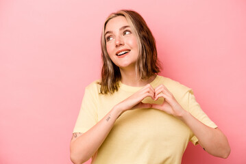 Fototapeta premium Young caucasian woman isolated on pink background smiling and showing a heart shape with hands.