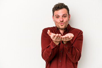 Young caucasian man isolated on white background folding lips and holding palms to send air kiss.