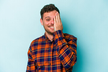 Obraz premium Young caucasian man isolated on blue background having fun covering half of face with palm.