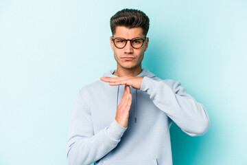 Young caucasian man isolated on blue background showing a timeout gesture.