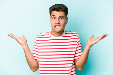 Young caucasian man isolated on blue background confused and doubtful shrugging shoulders to hold a copy space.