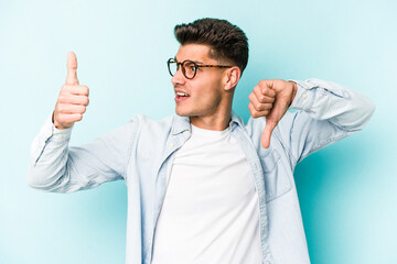 Young caucasian man isolated on blue background showing thumbs up and thumbs down, difficult choose...
