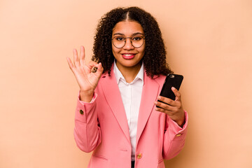 Young African American woman holding mobile phone isolated on beige background cheerful and...