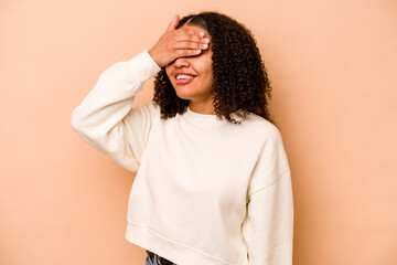 Young African American woman isolated on beige background covers eyes with hands, smiles broadly waiting for a surprise.