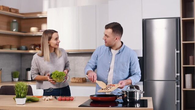 Using frying pan. Young couple is on the kitchen at home at daytime together