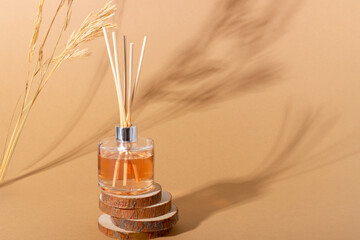reed diffuser bottle on the podium. Incense sticks for the home with a floral scent with hard shadows. The concept of eco-friendly fragrance for the home - obrazy, fototapety, plakaty