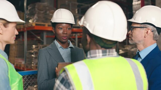 Close up of workers talking to businessmen standing in warehouse. Beautiful female boss using tablet device talking to male and female employees in retail construction storehouse, business concept