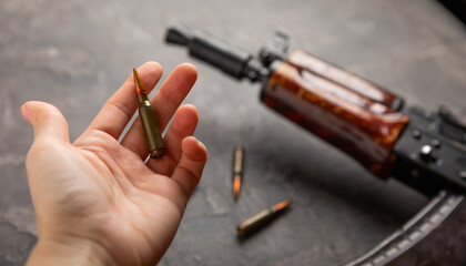A bullet in a woman's hand against the background of a military body armor, helmet and Kalashnikov...