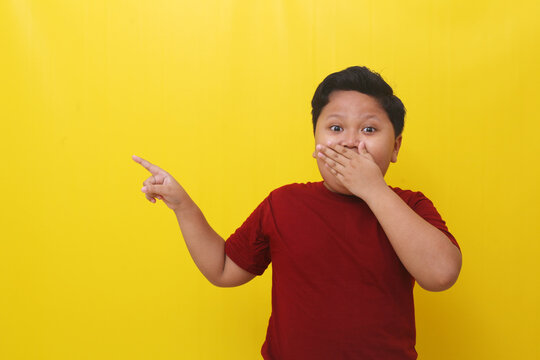 Wow expression of asian boy while standing and pointing something beside him. Isolated on yellow