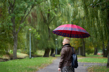 Portrait of stylish cute short haired blonde woman walking in the autumn park with red umbrella....