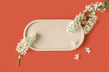 Podium for product presentation. Abstract minimal geometrical form on red orange background. Oval stone form, white flowers, soft shadow. Scene, Showcase, display. Minimal design. Top view, Flat lay