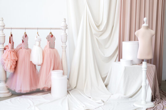 Baby dresses in pink shades on a hanger next to a mannequin in a studio with fabrics. Manufacture of wearing apparel