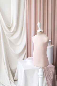 Baby mannequin in pink pastel color in the atelier studio on the background of fabrics of light shades.
