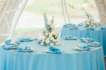 Wedding tables for guests. Round tables with a blue tablecloth. Decorated with flowers, plates, glasses and more