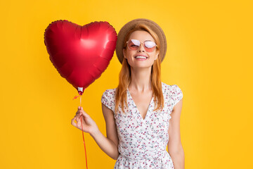 young woman smile in straw hat and sunglasses hold love heart balloon on yellow background
