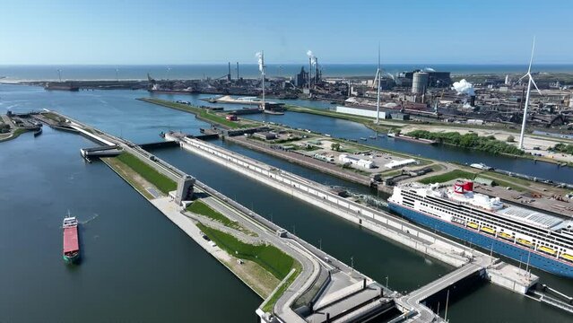 4k aerial video of cruise ship leaving large sea sluice towards Amsterdam in the Netherlands. Tata steel factory in the back ground