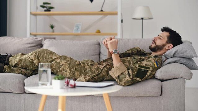 Side view. A soldier in Ukrainian uniform is laying down on the sofa and talking. Psychotherapy session