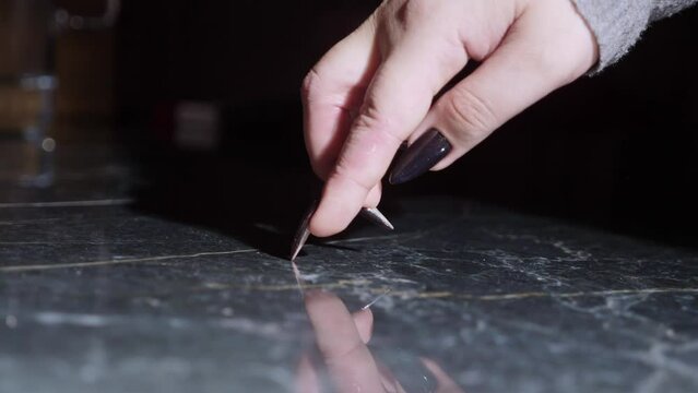 close-up, female fingers with long black nails step on a black reflective surface.