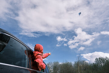 Preschool girl in red jacket launches kite from black car. Outdoor activity.