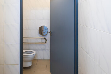 Flush toilet with metal holder. There is a toilet paper holder on the wall.