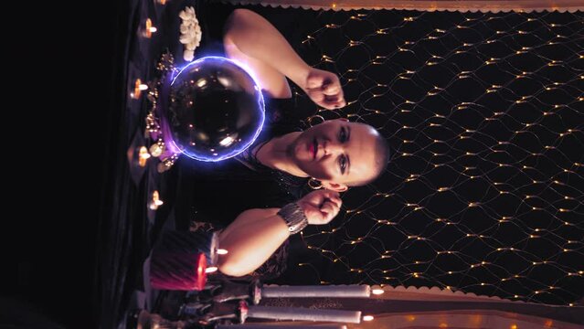 A bald fortune-teller in a magic salon tells fortunes in the salon on the table, a crystal ball electrified by lightning. vertical video