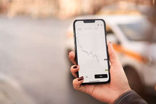 Female hand holding a mobile phone with graph doing down - stock market concept. Template for web design or app presentation. Gadget closeup. Digitalization, business, trading, crypto currency 