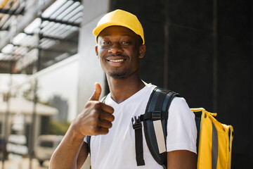 Food delivery, portrait of courier african man with yellow backpack and cap showing thumb up. Quick...
