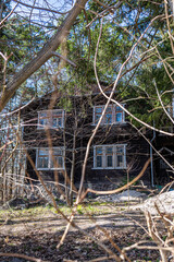 A wooden two-storey house with windows is located behind trees and shrubs in Svetlogorsk Raushen, Kalinigrad region, Russia, near the Baltic sea.