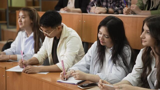 A group of students is studying in a lecture hall. Young people are studying at the university or a student is sitting in a school lesson. Teenagers listen to the teacher and write in the classroom.