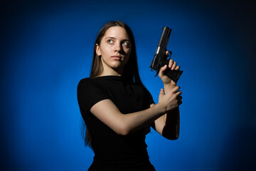 young beautiful woman with long hair in a black t-shirt with a gun on a blue background